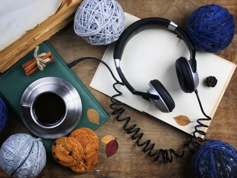 Et par høretelefoner ligger på et bord med kaffe og garnnøgler